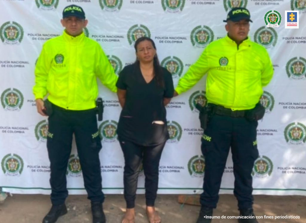 En la fotografía aparece una mujer capturada, en compañía de dos uniformados de la Policía Nacional. En la parte posterior un banner con logos de la entidad.