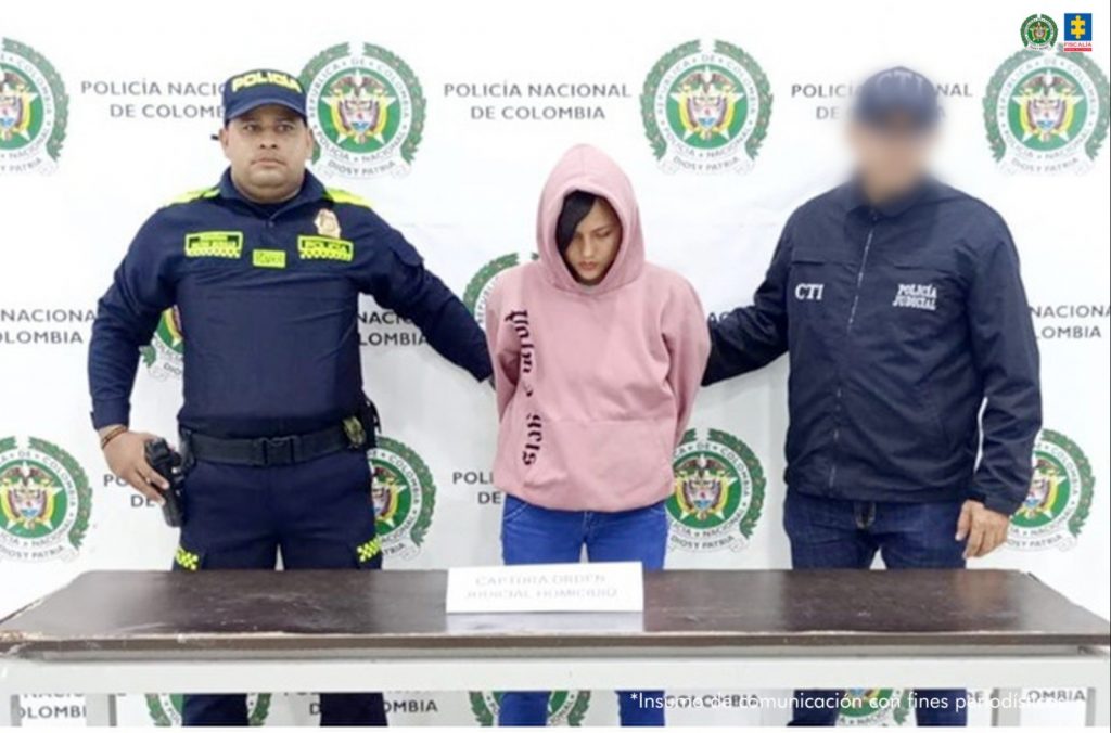 En la imagen aparece una mujer de buso de capota rosado y jean, entre dos uniformados del CTI y de la Policía Nacional.
