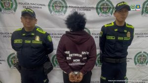 En la fotografía aparece de pie, de espaldas a la cámara, con los brazos atrás y esposada, Luz Mary Bonilla Mosquera. Viste con buso de manga larga y capucha de color vinotinto con estampados de palabras en color blanco; pantalón negro y zaptos grises. Usa el cabello tipo afro. En sus extremos hay uniformados de la Policía Nacional. En la parte posterior, hay un pendón institucional de la Policía.