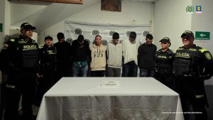 e observan seis personas capturadas, en fila y de frente. A cada costado, dos funcionarios de Policía Nacional. Adelante, una mesa con el letrero que dice CAPTURA ORDEN JUDICIAL. Atrás, un pendón de Policía Nacional