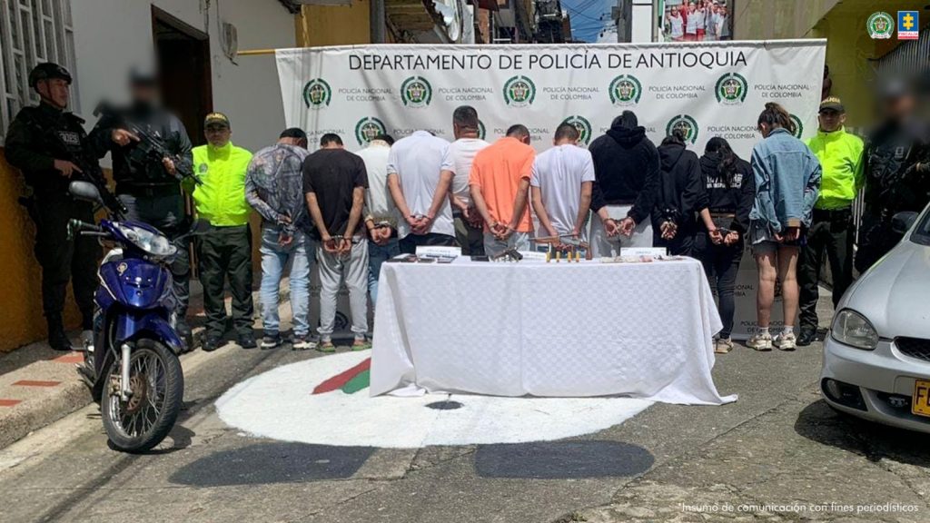 En la imagen aparecen los procesados en medio de servidores del cti y la policía nacional. También aparecen un automóvil, una moto, dos armas de fuego y dinero en efectivo.