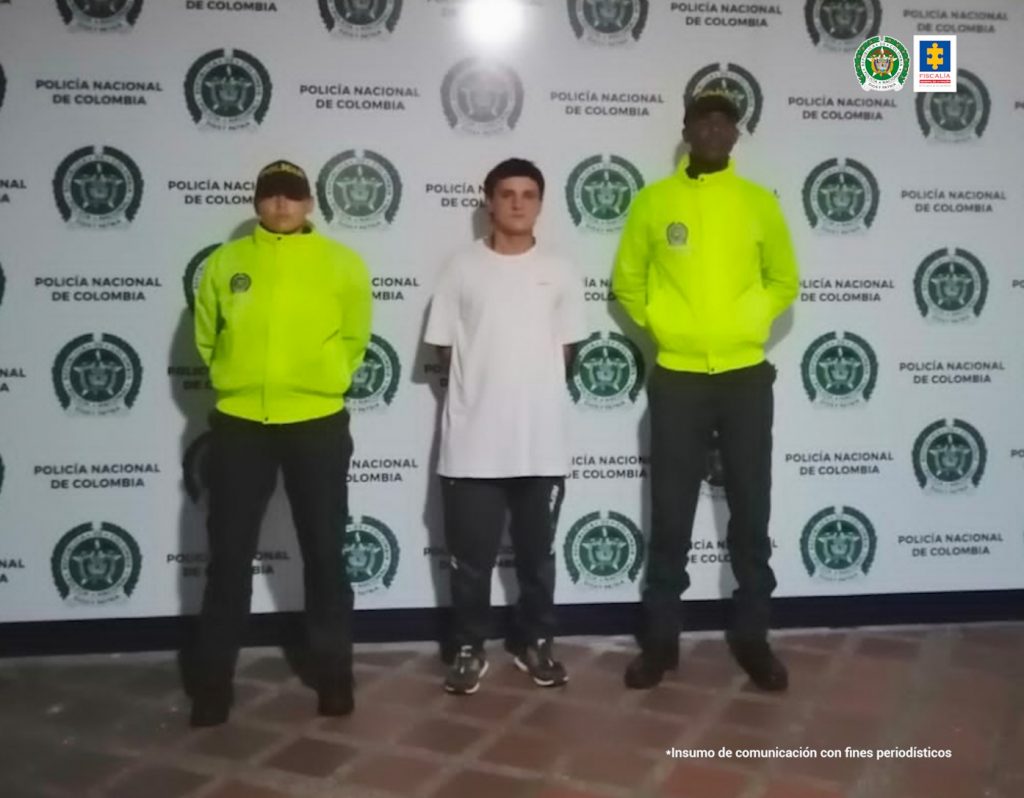 Se observa en el centro al detenido de frente y en cada costado un funcionario de Policía Nacional. Atrás un pendón de Policía Nacional