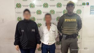 En la fotografía aparece de pie y con los brazos atrás el hoy imputado. Viste con camisa de manga larga, de color blanco, jean azul oscuro y botas negras. A su extremo derecho hay una servidora del CTI de la Fiscalía y al derecho un uniformado de la Policía. Detrás de ellos hay un pendón institucional de la Policía.