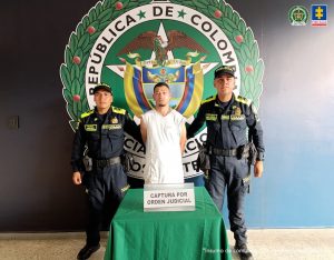 En la fotografía se aprecia de pie y con los brazos atrás a Maicol Lisandro Gutiérrez Tangarife. Usa barba tipo chivera corta. Viste camiseta blanca de manga corta. A los extremos de ellos hay uniformados de la Policía Nacional. Delante de ellos hay una mesa con mantel verde y sobre ella hay un letrero que dice. ‘Captura por orden judicial’. Detrás de ellos hay un pendón institucional de la Policía.