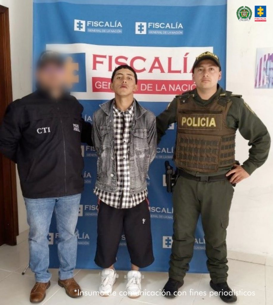 En la fotografía aparece de pie y con los brazos atrás Maiker Nicolás Romero Cardona. Viste con chaqueta de jean de color gris, camisa de cuadros negros con blanco, bermuda de color negro y zapatillas blancas. Al extremo derecho hay un servidor del CTI de la Fiscalía y al extremo izquierdo un uniformado de la Policía Nacional. Detrás de ellos hay un pendón institucional de la Fiscalía.
