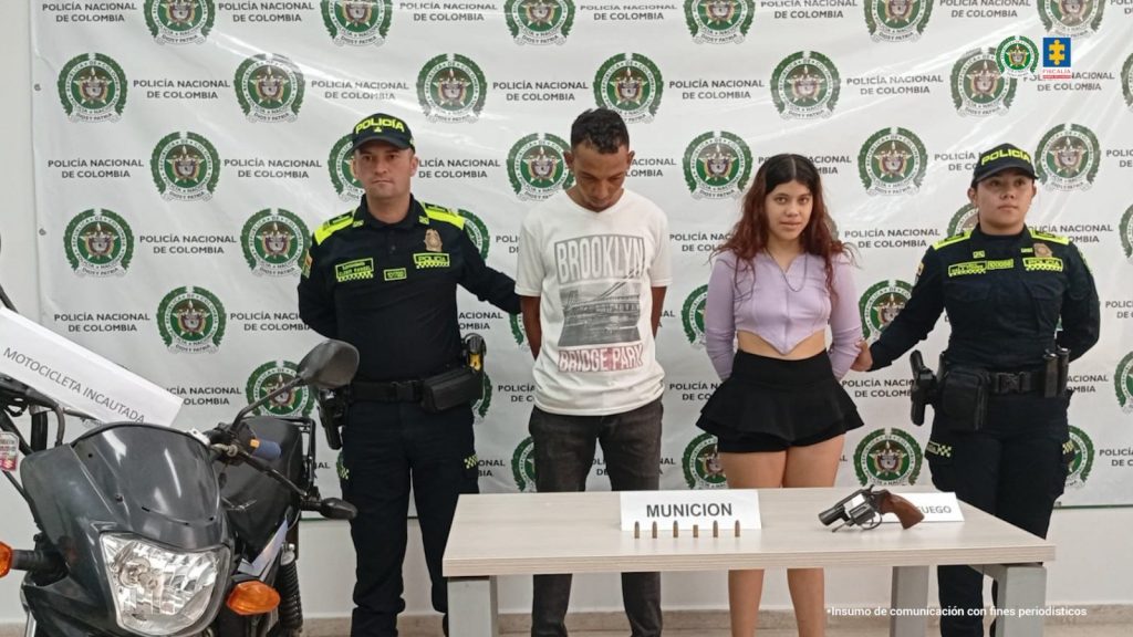 Se visualiza a los capturados junto a dos uniformados de la Policía Nacional. Frente a ellos los elementos incautados (revolver- munición) y la motocicleta hurtada. Detrás de ellos el banner que identifica a la Policía Nacional.