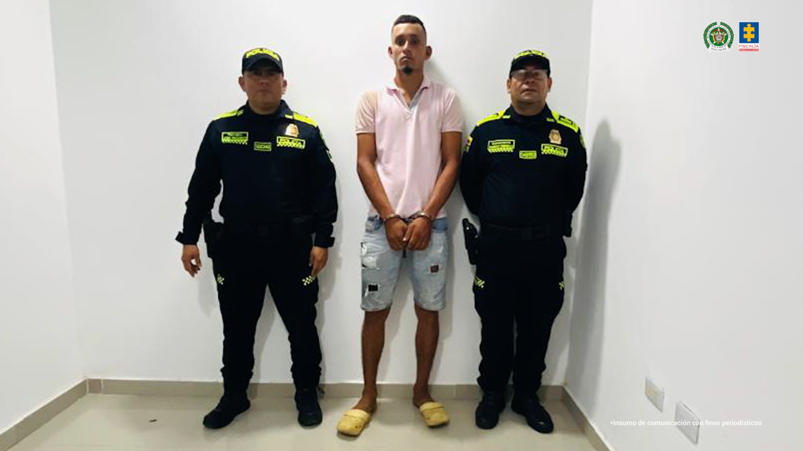 En la imagen aparece una persona de camiseta rosada y bermuda de jean, entre dos uniformados de la Policía.