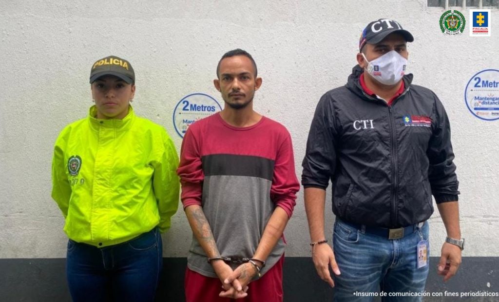 En la foto aparece Manuel Fernando Peláez Maza, alias ‘Soldado’, con los brazos adelante y esposado. Viste buzo de manga larga vinotinto con gris y con franja negra en el pecho; pantalón vinotinto. A su derecha hay una uniformada de la Policía Nacional y a la izquierda de él un servidor del CTI de la Fiscalía.