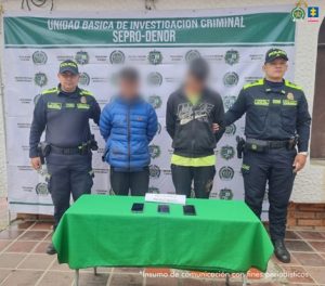 Se visualiza a los capturados junto a uniformados de la Policía Nacional. Frente a ellos una mesa con los teléfonos incautados. Detrás de ellos el banner que identifica a la Policía Nacional