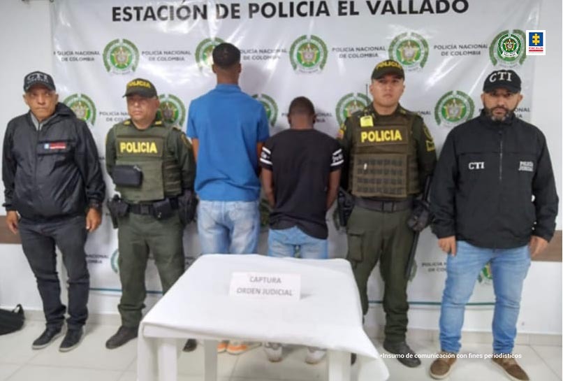 En la fotografía aparecen dos personas capturadas, junto a un servidor del CTI y un agente de la Policía Metropolitana de Cali. En la parte posterior de la imagen se ve un banner de la Policía Nacional