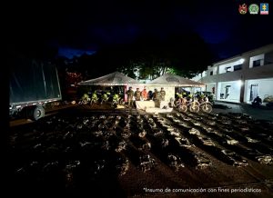 La fotografía fue tomada en la noche y se aprecia a lo lejos a María Alejandra Angulo Osorio y Luis Ángel Bernal Arango. A sus extremos hay uniformados del Ejército y de la Policía Nacional. Delante de ellos hay una mesa con mantel blanco y sobre ella se ven algunos elementos. Sobre el piso hay paquetes de prendas y al extremo derecho se ve la parte posterior de un camión. En la parte posterior, debajo de dos carpas blancas con logos de la Policía, se encuentran los judicializados y los uniformados, así como dos pendones institucionales del Ejército y Policía.
