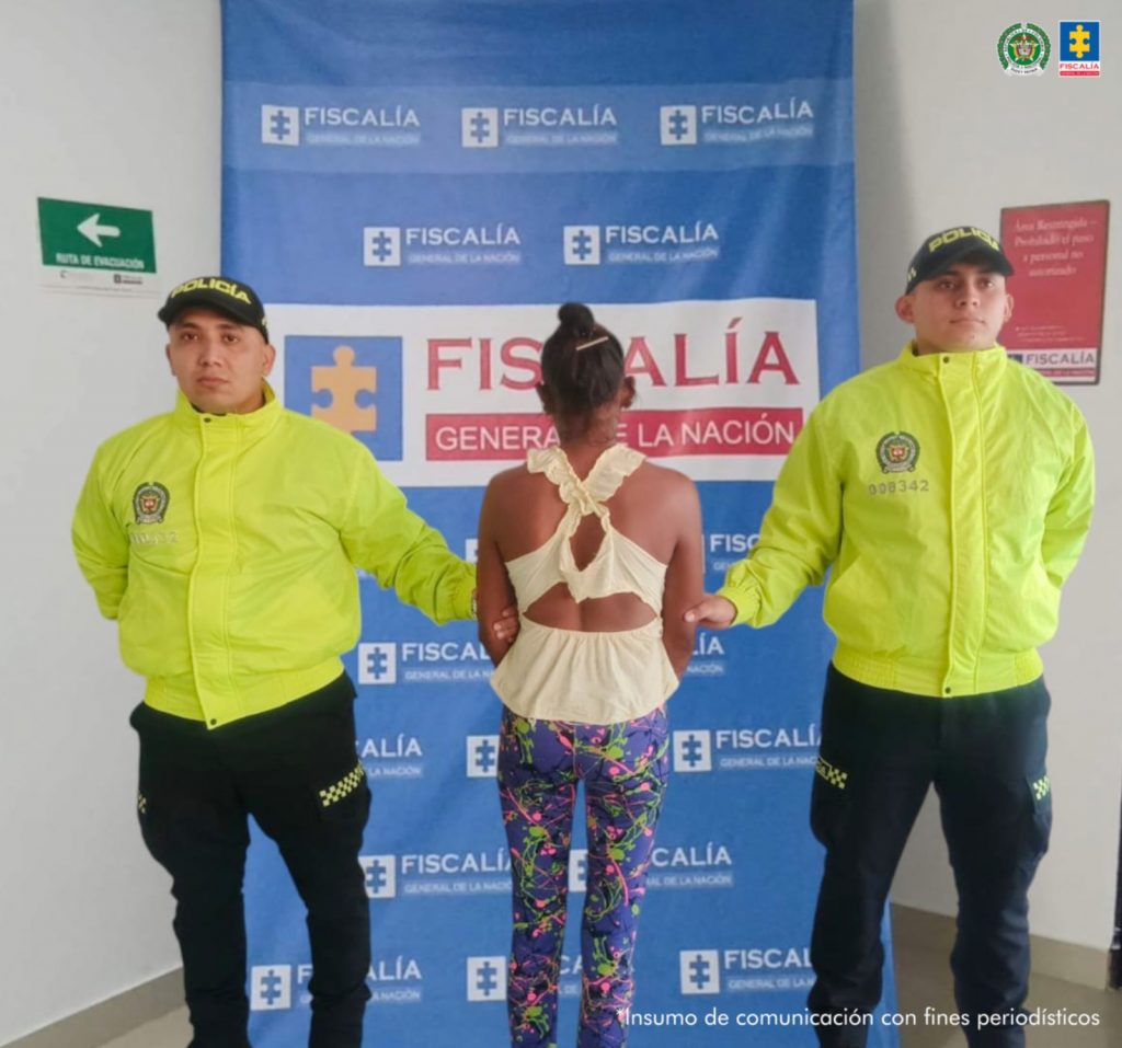 Se visualiza al capturada de espaldas junto a un uniformado de la Policía Nacional. Detrás de ellos el banner que identifica a la Fiscalía General de la Nación.