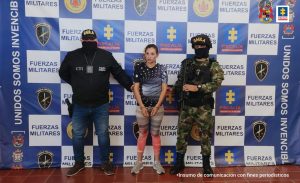 capturada de frente esposada manos al frente custodiada por investigador de Fiscalía y militar del grupo Gaula. Detrás banner conjunto .