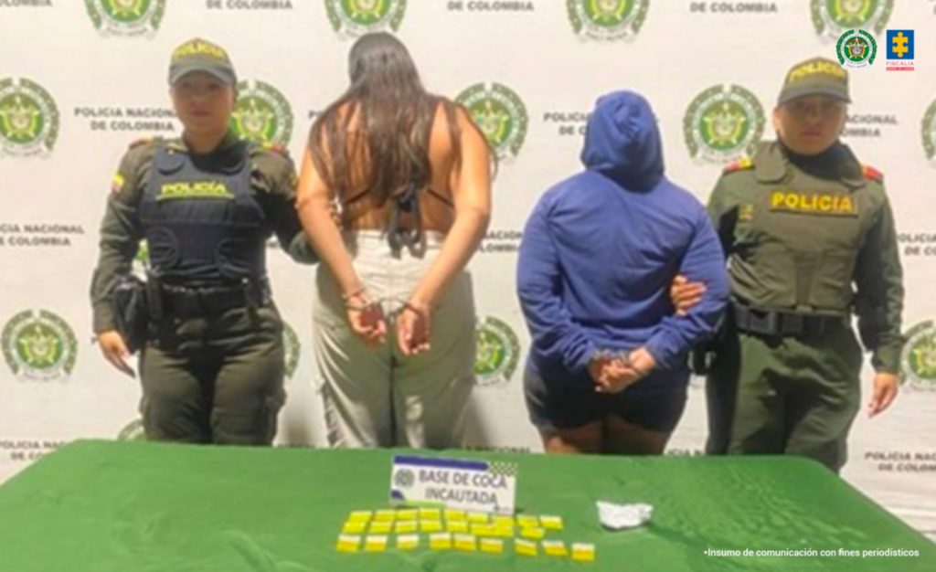 En la fotografía aparecen de espaldas a la cámara Martha Cecilia Marín Correa y Daniela Ríos Duque. Una viste buso azul y capucha, short de color azul. La otra mujer viste blusa negra descubierta atrás y pantalón beage con bolsillos a los lados a la altura de los muslos. Delante hay una superficie verde y sobre ella se ven bolsas plásticas de color amarillo y un letrero que dice: ‘Base de coca incautada’. En la parte posterior hay un pendón institucional de la Policía.