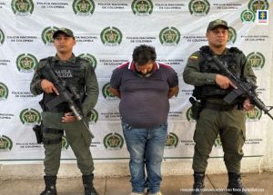 En la fotografía aparece un hombre capturado, acompañado de dos uniformados de La Policía. En la parte posterior un banner con logos de la entidad.