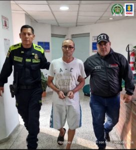 En la fotografía se aprecia en un pasillo, en acción de caminata y con los brazos atrás a José Luis Restrepo Peláez. Viste camiseta blanca con letras mayúsculas estampadas; bermuda blanca con franjas azules y pantuflas oscuras. Al lado izquierdo de él hay un servidor del CTI de la Fiscalía y al lado derecho un uniformado de la Policía Nacional.