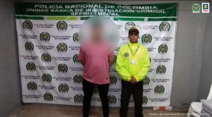 En la fotografía se aprecia de pie y con los brazos atrás a Rosemberg Mauricio Cortés Lozano. Viste camisa rosada y pantalón negro. Al lado izquierdo de él hay un uniformado de la Policía Nacional. Detrás de ellos hay un pendón institucional de la Policía Nacional.