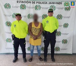 Fiscal Mancera, Fiscal Martha Mancera, Martha Mancera, Fiscalía General de la Nación En la fotografía se aprecia de pie, con los brazos adelante y esposado, a Yanier Alfredo Micolta. Viste camisa esqueleto amarilla con estampado negro en la parte abdominal, jean azul desgastado y pantuflas negras. A lado y lado de él hay uniformados de la Policía Nacional. Detrás de ellos hay un pendón institucional de la Policía. Detrás de ellos hay un pendón institucional de la Policía.