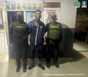 Fiscal Mancera, Fiscal Martha Mancera, Martha Mancera En la fotografía esta un hombre delgado, de pie, con los brazos atrás, moreno, vestido de chaqueta azul con negra, jean y tenis negro, custodiado por dos uniformados de la Policía Nacional.