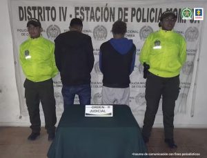 Fiscal Mancera, Fiscal Martha Mancera, Martha Mancera En la imagen están dos hombres de espalda, con los brazos hacía adelante, uno vestido de buzo negro con jean azul y el otro con buzo azul con negro y pantalón blanco. Se encuentran acompañados de dos agentes de la Policía Nacional. Detrás de ellos hay un pendón de esa institución.