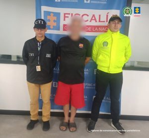 Se visualiza al capturado con el rostro difuminado junto a un investigador del CTI y un integrante de la Sijin. Detrás el banner que identifica a la Fiscalía General de la Nación