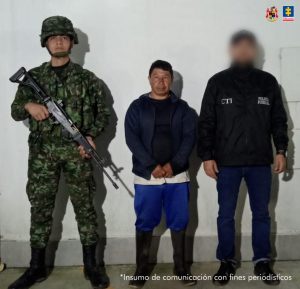 En la imagen se ve al capturado en custodia por el servidor del CTI y un uniformado del Ejército Nacional. El capturado tiene un pantalón azul, con botas negras y una chaqueta negra