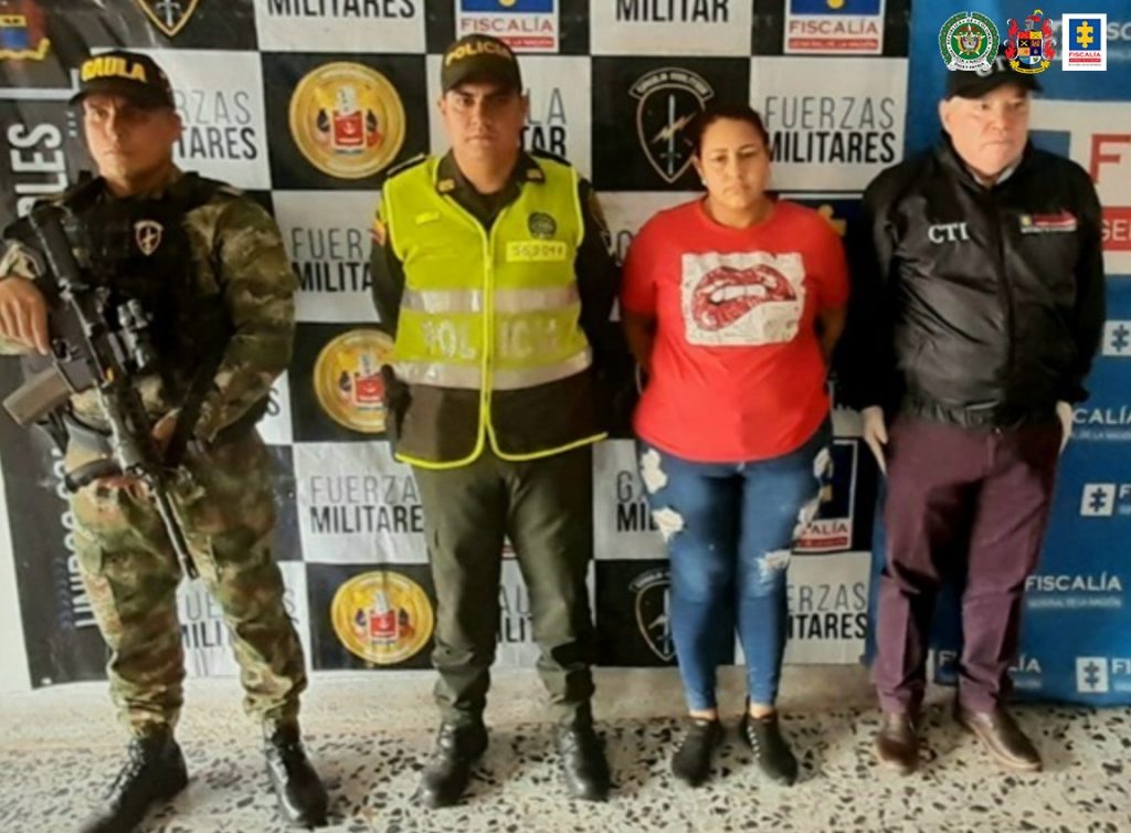 En la imagen se ve una mujer detenida con tres funcionarios del CTI, el Ejército y la Policía Nacional. Detrás suyo hay dos pendones de la Fiscalía y el Ejército.