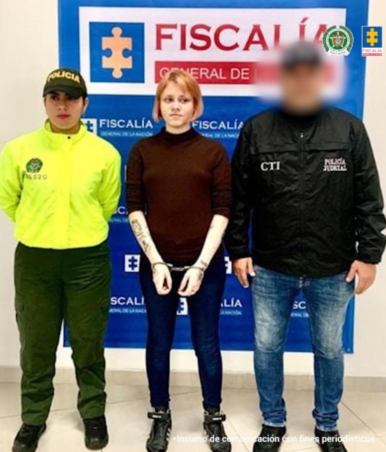 Se observa la capturada de frente. A un costado un funcionario del Cuerpo Técnico de Investigación (CTI) y al otro uno de Policía nacional. Al fondo un pendón de la Fiscalía General de la Nación