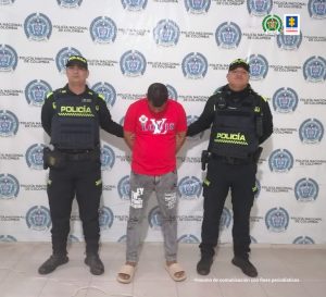 En la fotografía aparece una persona capturada, acompañado de dos uniformados de La Policía. En la parte posterior un banner con logos de la entidad.
