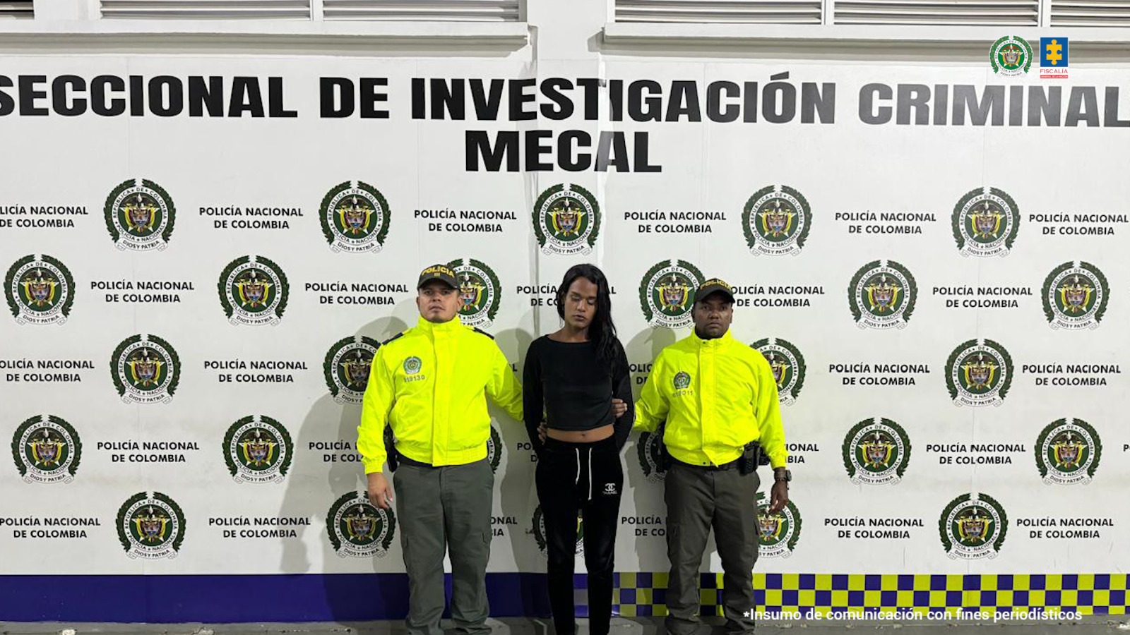 En la fotografía se aprecia de pie y con los brazos atrás a Michelle. Viste blusa de manga larga y pantalón de sudadera de color negro. A sus extremos hay uniformados de la Policía Nacional. Detrás de ellos hay un pendón institucional de la Policía.