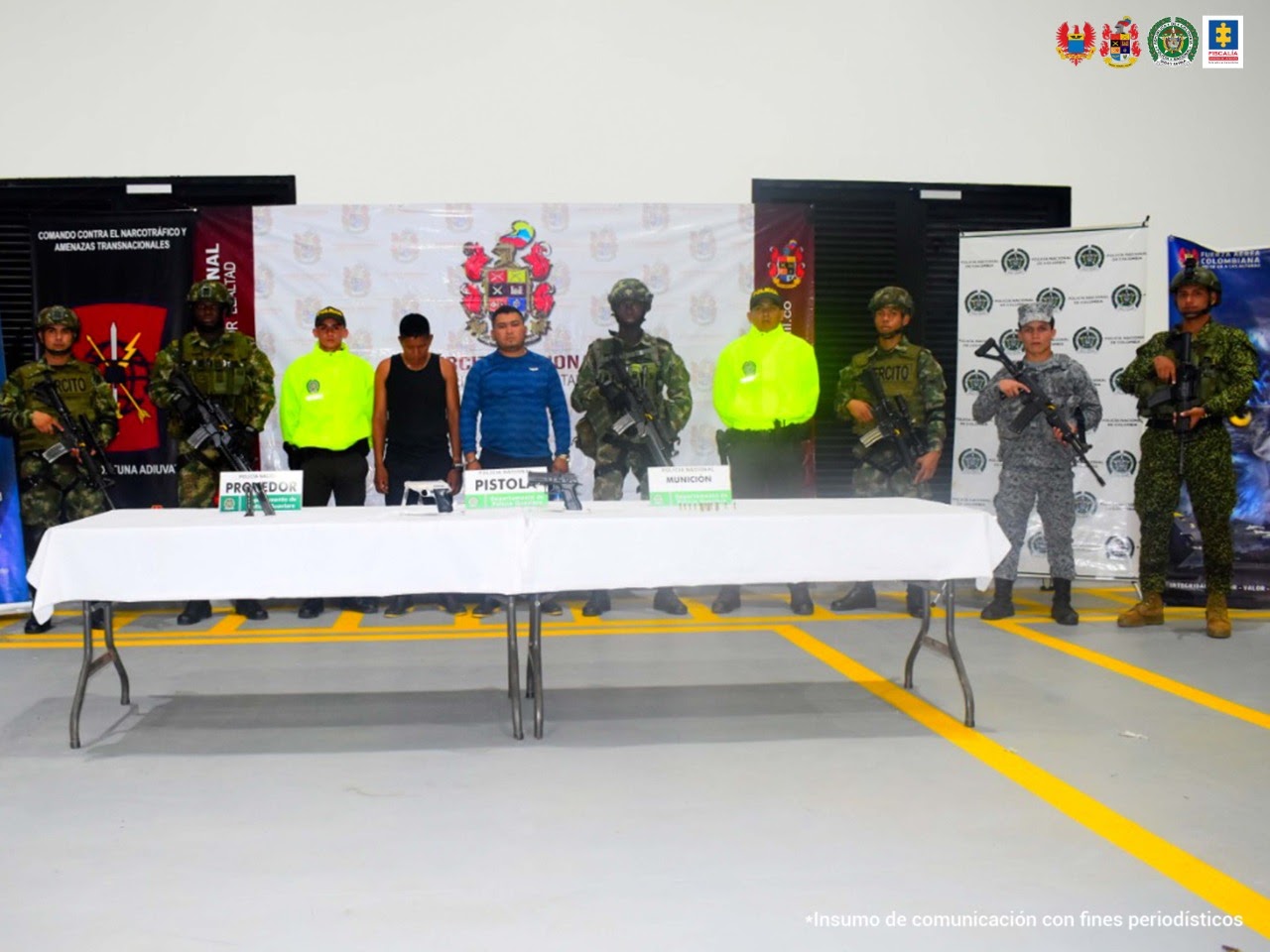 En la foto se ven los dos hombres capturados en el centro de la imagen custodiados por uniformados de Ejército, Policía y Fuerza Aérea, detrás los banners de cada institución militar y delante de ellos, una mesa con el material incautado.
