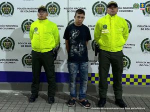 En la fotografía se aprecia de pie y con los brazos atrás a Miguel Ángel Moreno Ocampo. Viste camisa de manga corta de color negro con estampado blanco; jean azul desgastado y pantuflas negras. A sus extremos hay uniformados de la Policía Nacional. Detrás de ellos hay un pendón institucional de la Policía.
