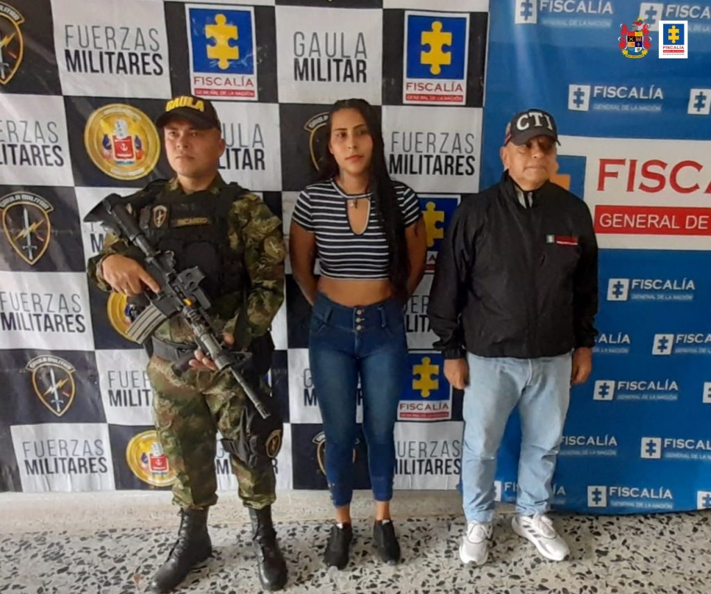 En la imagen se ve una mujer detenida con un funcionario del CTI y otro del Ejército. Al fondo dos pendones de la Fiscalía y el Ejército.