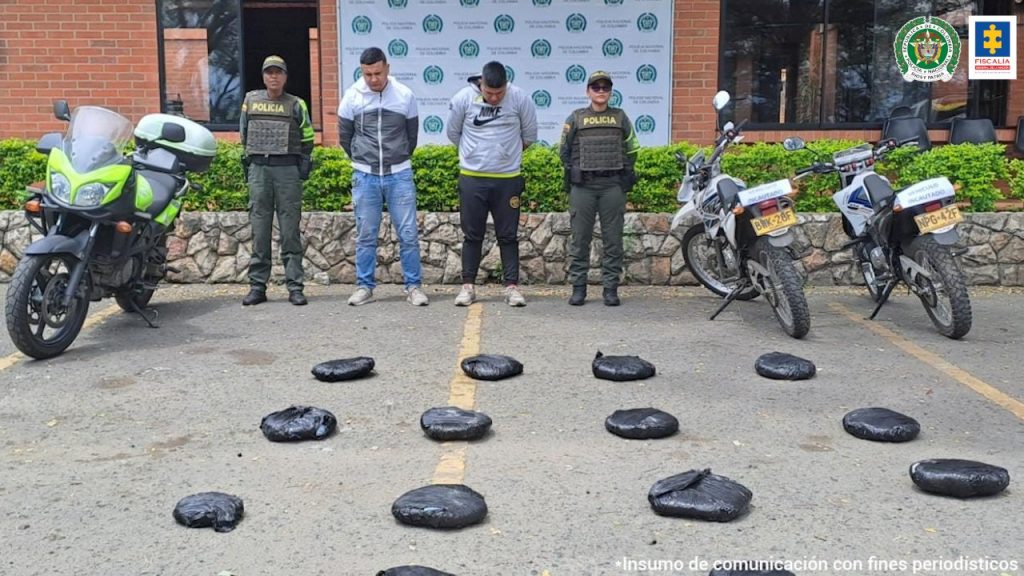 En la foto aparecen de pie Julio César Córdoba Hernández y Maykol Stiven Gaviria Daza. A lado y lado de ellos hay dos uniformados de la Policía Nacional; tres motocicletas (una de ellas de la Policía) y delante de ellos, sobre el piso, hay 14 paquetes negros. Detrás de los judicializados y los policiales se aprecia un pendón institucional de la Policía. 
