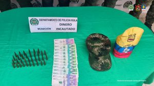 En la imágen se observa una mesa de color verde, donde se puede observar la munición, el dinero en efectivo, la gorra y el brazalete alusivo a las extintas Farc.