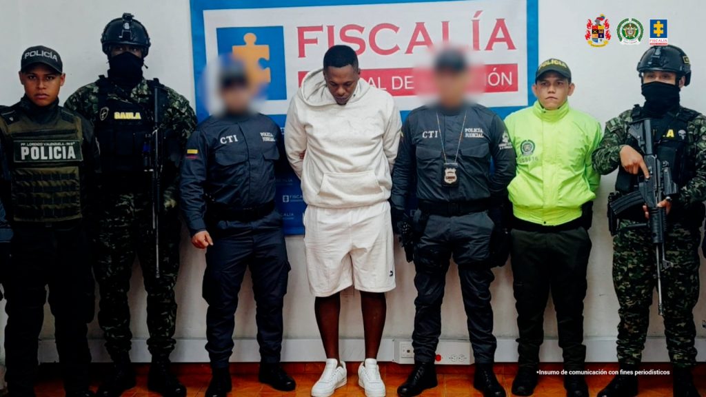 En la fotografía aparece de pie y con los brazos atrás Neftaly Hurtado Rivas. Viste buso y bermuda de color beage, así como zapatillas blancas. A sus extremos hay servidores del CTI de la Fiscalía; así como de la Policía y Ejército Nacional. Detrás de ellos hay un pendón institucional de la Fiscalía.
