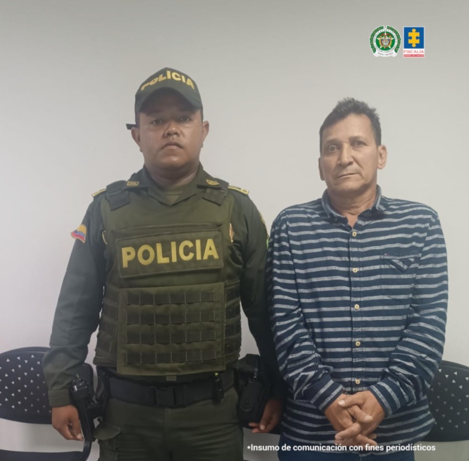 En la fotografía aparece de pie, con los brazos adelante y esposado, Nelson Enrique Rincón Ortiz. Viste camisa de manga larga, con rayas horizontales azules y grises; asimismo, jean azul. A su extremo derecho hay un uniformado de la Policía Nacional. Detrás de ellos hay tres sillas de color negro.
