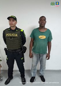 En la fotografía se aprecia de pie a Nelson Ordóñez Quiñónez. Viste camiseta de manga corta de color verde con impresión ovalada de color amarillo a la altura del pecho; jean azul claro desgastado y zapatillas negras con blanco. Al lado derecho de él hay un uniformado de la Policía Nacional.