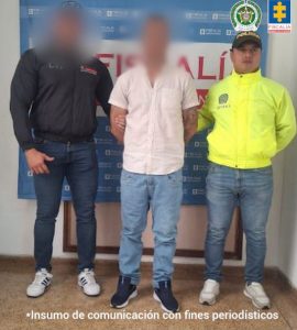 En la fotografía aparece de pie y con los brazos atrás el presunto implicado. Usa barba tipo ‘chivera’. Viste con camisa de color beage, manga corta y de botones; jean azul y zapatillas negras con zuela de color blanco. A su extremo derecho hay un servidor del CTI de la Fiscalía y al extremo izquierdo un uniformado de la Policía Nacional. Detrás de ellos hay un pendón institucional de la Fiscalía.
