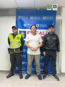 Fiscal Martha Mancera, Martha Mancera, Fiscal Mancera el capturado esta de frente esposado custodiado por investighador del CTI de la Fiscalía y por un policía. Detrás banner de Fiscalía.