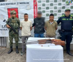 En la foto aparece dos de los capturados custodiados un sevidor del CTI y dos uniformados de la Policía Nacional. En la foto también aparece de fondo un backing de la Policía Nacional. En la foto aparecen tres armas de fuego incautadas.