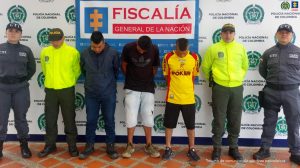 Se observan tres personas capturadas en fila. A cada costado funcionarios del Cuerpo Técnico de Investigación CTI y de la Policías Nacional.Atrás, un pendón de Fiscalía General de la Nación y uno de Policía Nacional