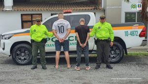 en una foto se observan dos capturados de espaldas y un oficial de la Policía Nacional en cada extremos de la fila. Atrás un vehículo de Policía Nacional.
