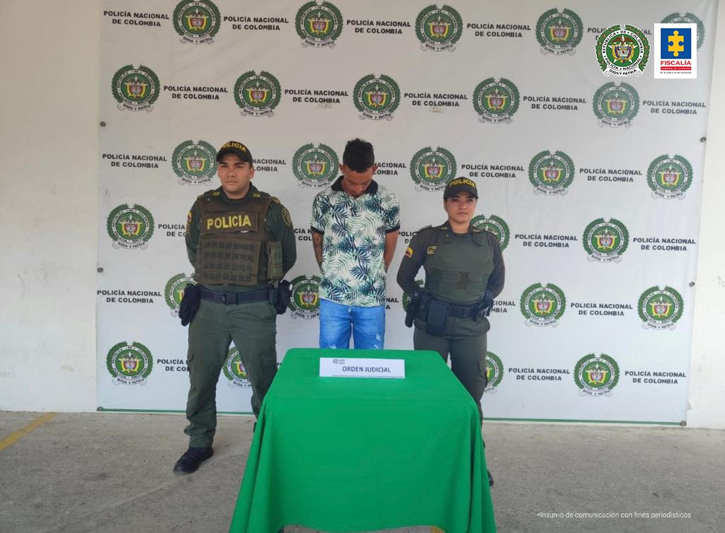 El capturado aparece esposado junto a dos uniformados de la Policía.