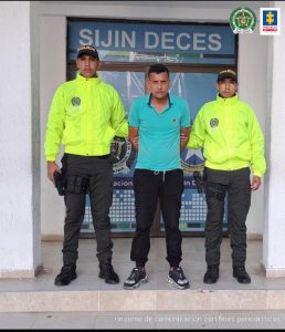 En la fotografía aparece un hombre capturado, acompañado de dos uniformados de la Policía. En la parte posterior un banner con logos de la entidad.