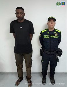 En la fotografía se aprecia de pie y con los brazos atrás a Oscar Mauricio Caicedo. Viste camiseta de manga corta y pantalón de color negro; así como zandalias negras. Al lado izquierdo de él hay un uniformado de la Policía Nacional.