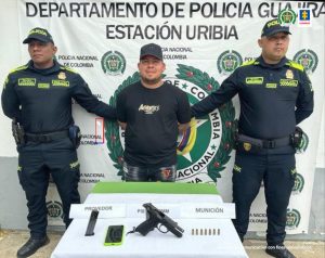 En la fotografía aparece un hombre capturado, acompañado de dos uniformados de la Policía Nacional. En la parte posterior un banner con el logo de la entidad.