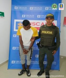 Se observa al capturado junto a uniformado de la Policía Nacional. En la parte posterior se ubica el banner que identifica a la Fiscalía General de la Nación.