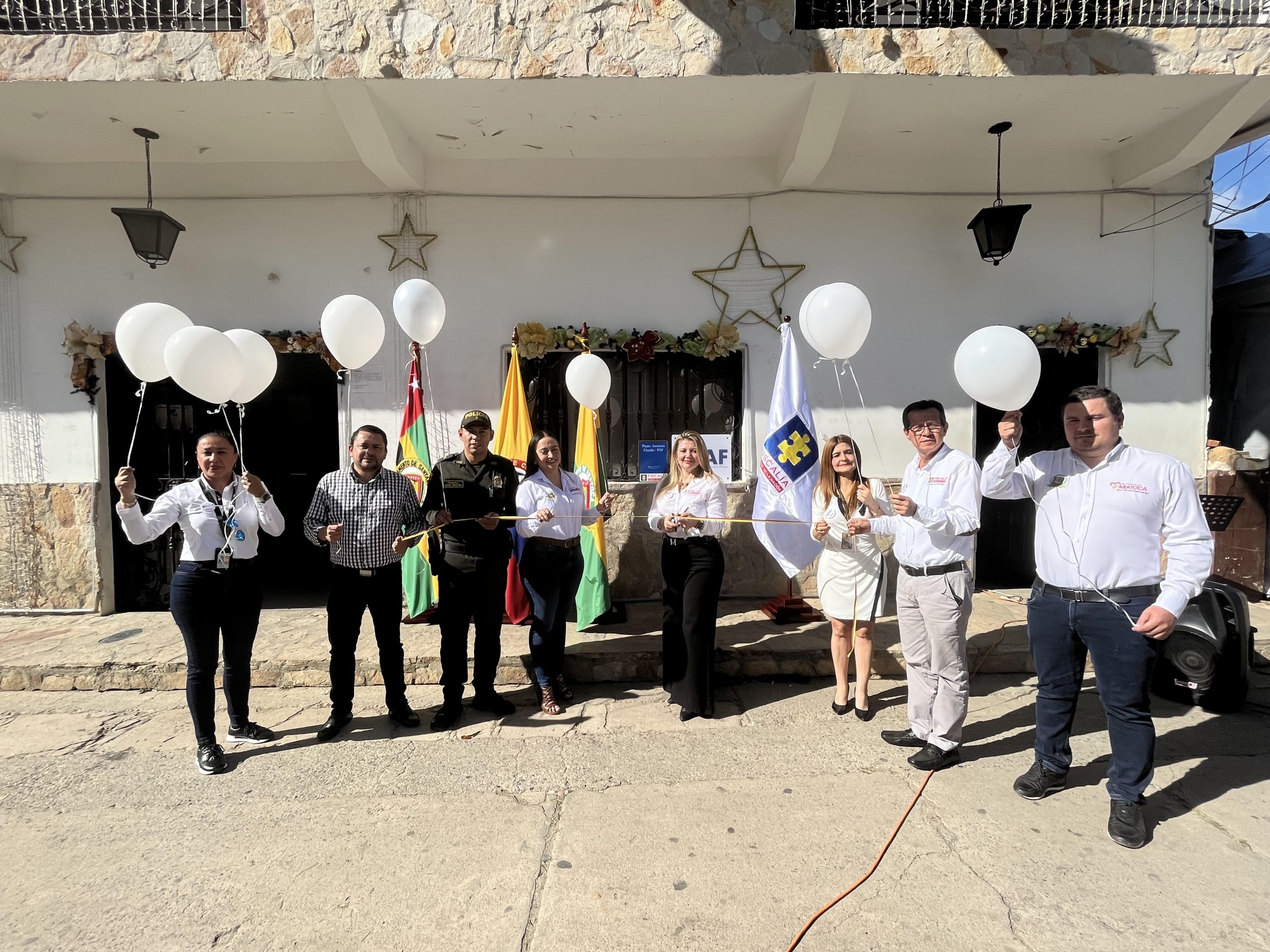 Frente a una casa varias personas posan con globos en sus manos. Al fondo se ve el PAF