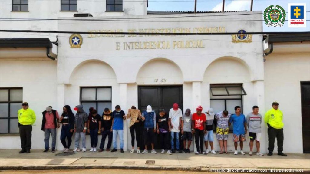 En la foto aparecen los 16 capturados, siendo custodiados por dos miembros de la Policía.